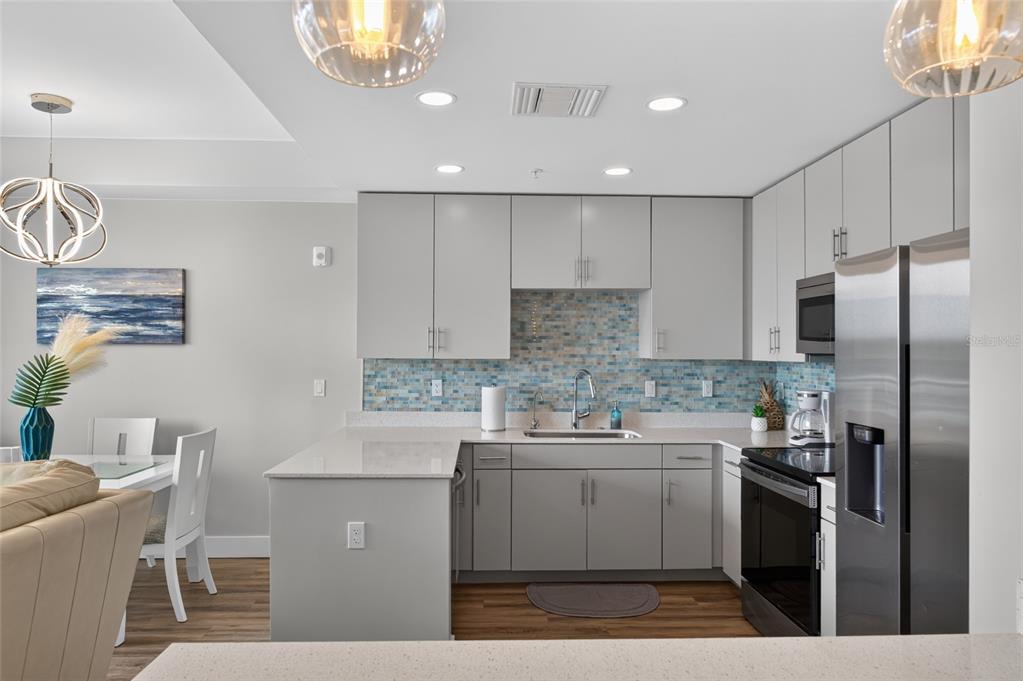 A modern kitchen features light gray cabinets, a blue mosaic backsplash, and stainless steel appliances — 1709 N TAMIAMI TRAIL UNIT 505, SARASOTA, FL