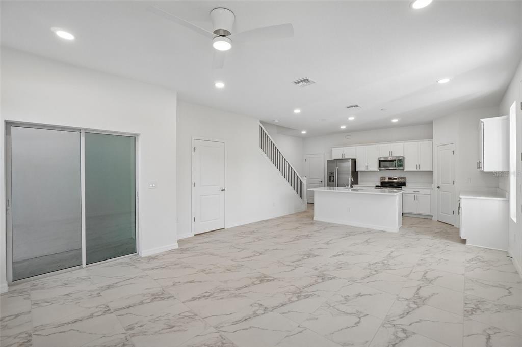 An open-concept kitchen and living area features white cabinetry, marble-look tile flooring, and a staircase — 613 SILVER STREAM COURT, BRANDON, FL