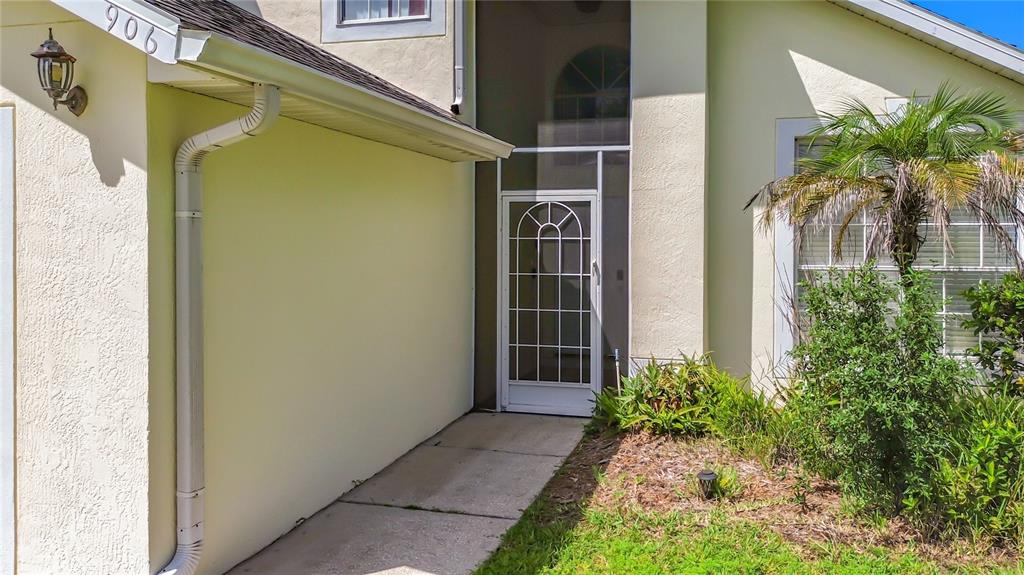 A beige house exterior features a white screen door, a concrete walkway, and a palm tree — 906 MONTANA AVENUE, DAVENPORT, FL