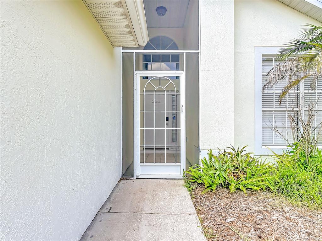 A white front door with a screen door sits under a covered entryway with stucco walls — 906 MONTANA AVENUE, DAVENPORT, FL