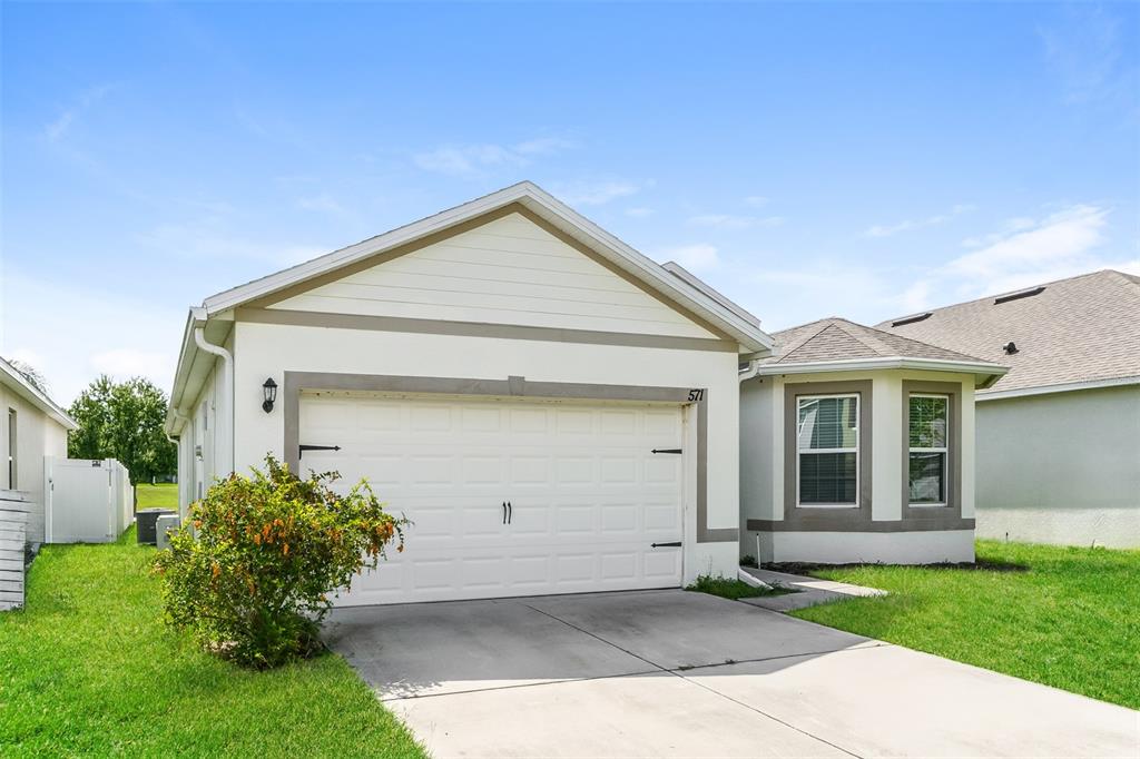 A single-story house with a white stucco exterior, a two-car garage, and a bay window — 571 AUTUMN STREAM DRIVE, AUBURNDALE, FL
