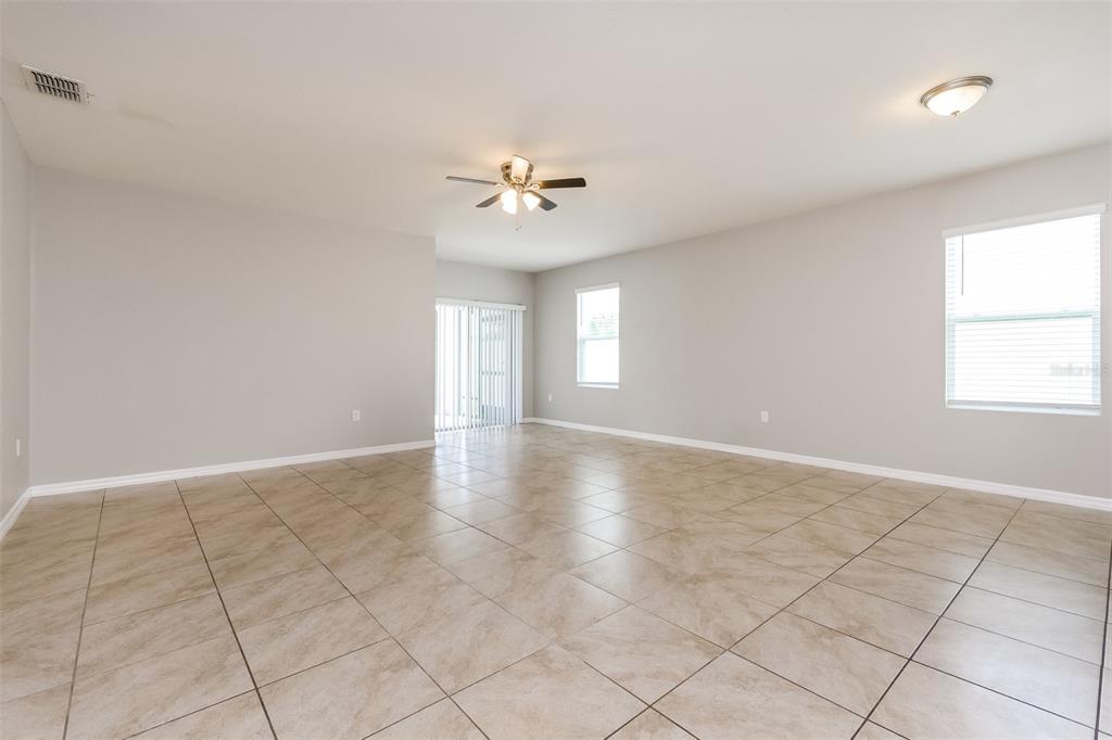 An empty living room features light-colored tile flooring, gray walls, and a ceiling fan — 571 AUTUMN STREAM DRIVE, AUBURNDALE, FL