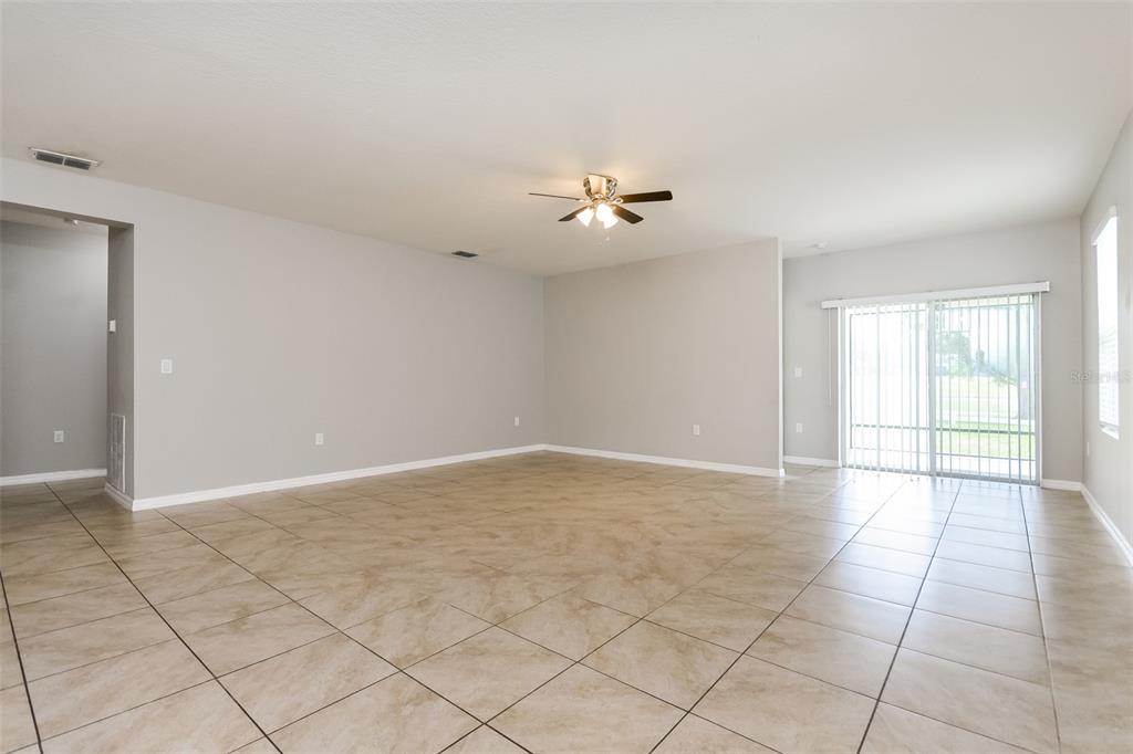 An open living area features light gray walls, large tan floor tiles, and a ceiling fan — 571 AUTUMN STREAM DRIVE, AUBURNDALE, FL