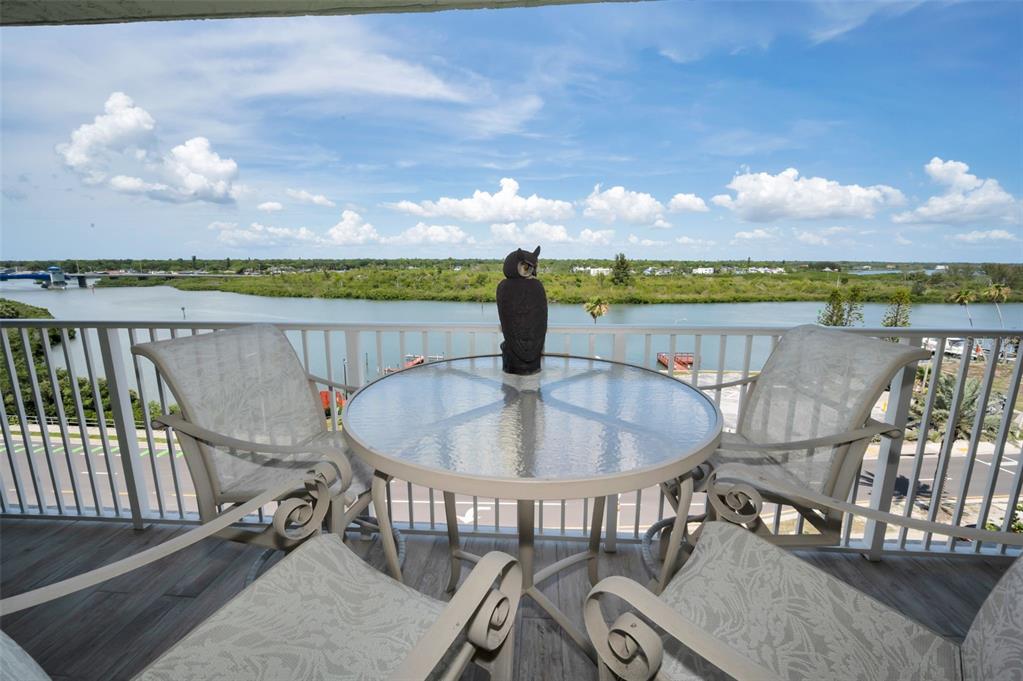 A balcony features a glass-topped table, four chairs, and an owl statue overlooking a waterway — 18610 GULF BOULEVARD UNIT 610, INDIAN SHORES, FL