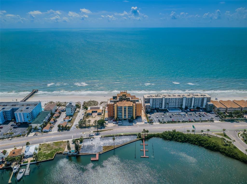 An aerial view shows a coastal area with a beach, ocean, and multi-story apartment buildings — 18610 GULF BOULEVARD UNIT 610, INDIAN SHORES, FL