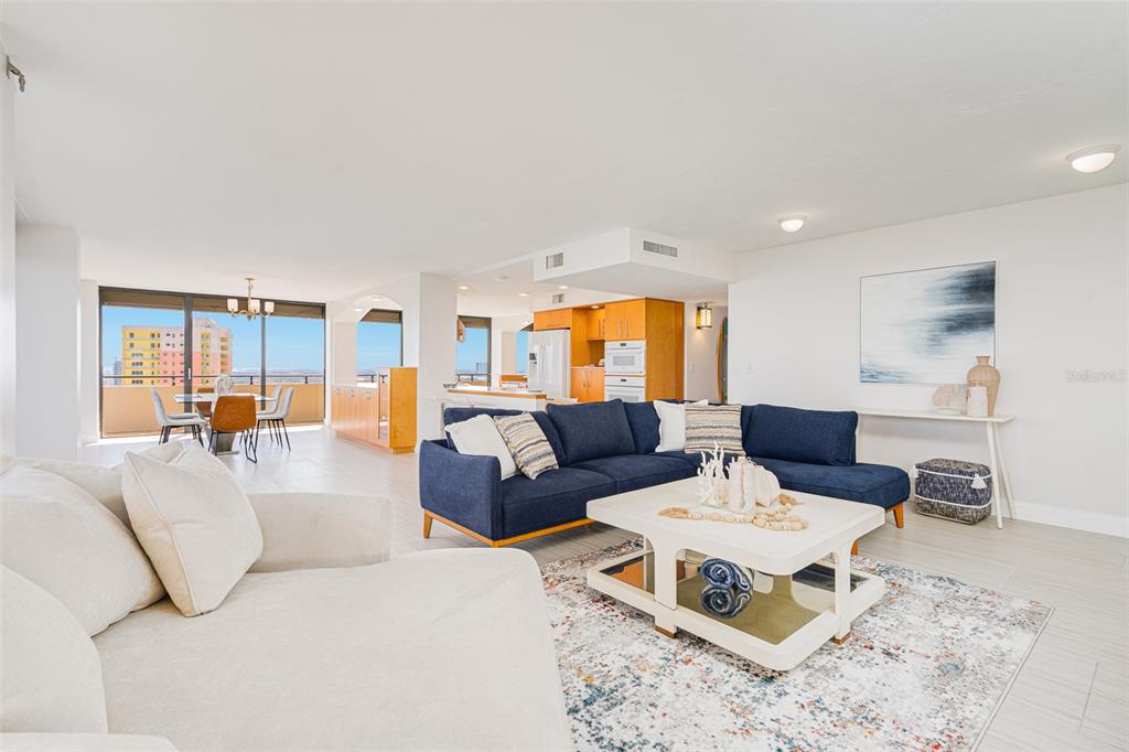 A bright open-concept living room features a blue sectional, white sofa, and a dining area — 2200 N ATLANTIC AVENUE UNIT 1502, DAYTONA BEACH, FL