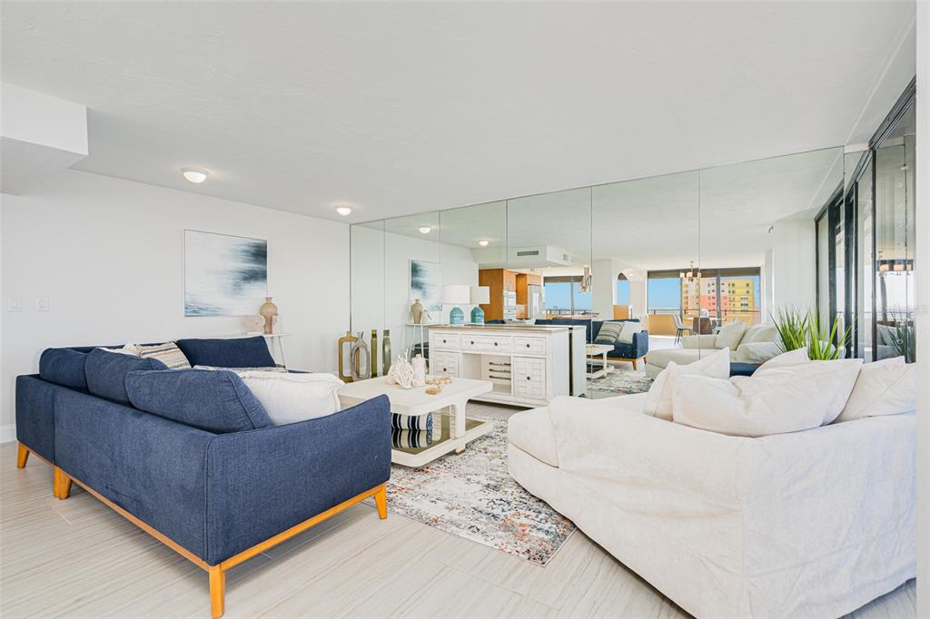 A living room features a blue sofa, white armchair, coffee table, and a mirrored wall — 2200 N ATLANTIC AVENUE UNIT 1502, DAYTONA BEACH, FL