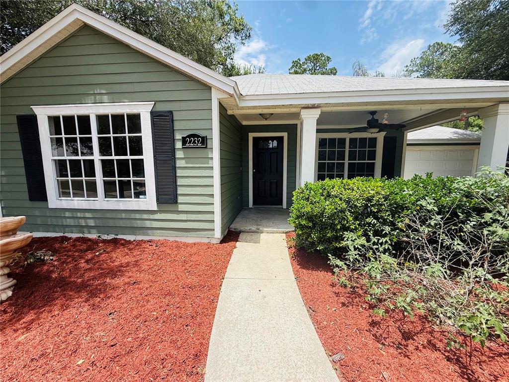 The exterior of a green house features a front porch, a walkway, and red mulch — 2232 NE 13TH AVENUE, GAINESVILLE, FL