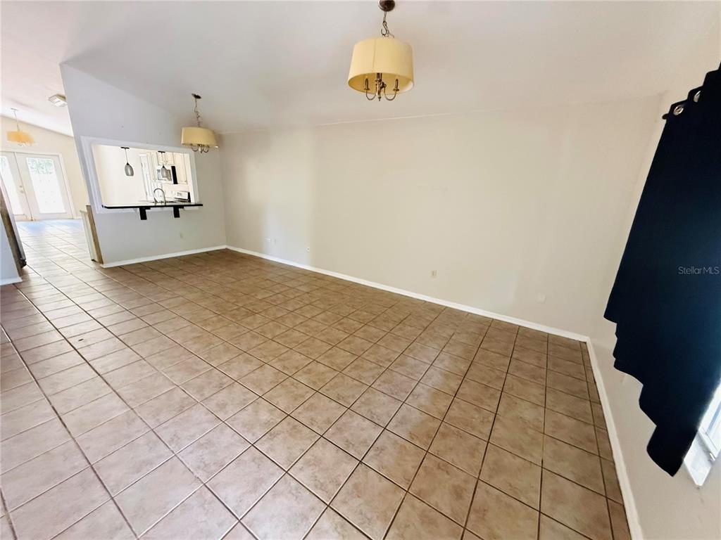 An empty room with tan tile flooring, two pendant lights, and a kitchen pass-through window — 2232 NE 13TH AVENUE, GAINESVILLE, FL