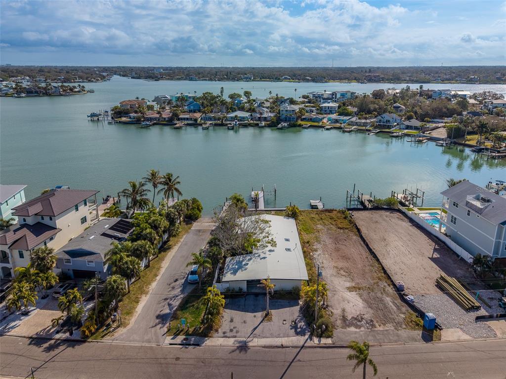 An aerial view shows a waterfront property with a house, a vacant lot, and docks — 1217 BAY SHORE BOULEVARD, INDIAN ROCKS BEACH, FL