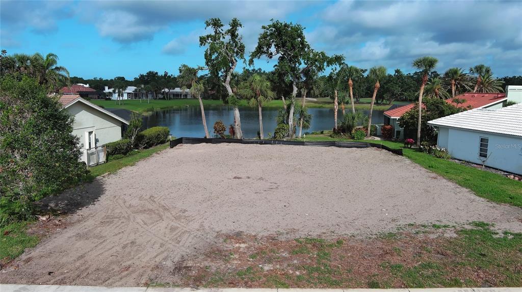 A vacant, sandy residential lot sits between two houses overlooking a small lake — 1717 KILRUSS DRIVE, VENICE, FL