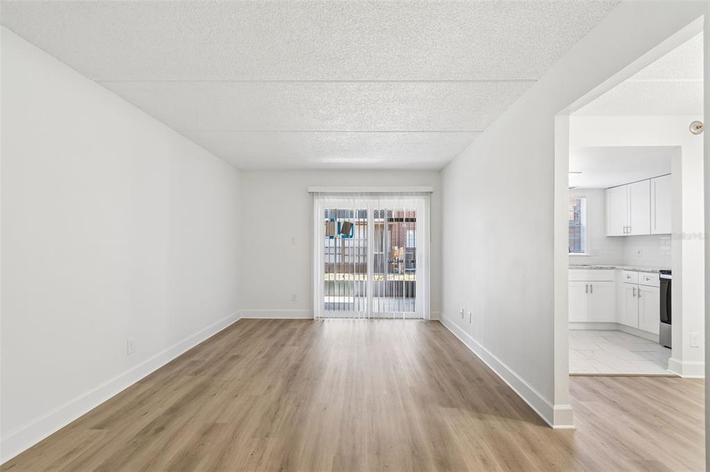 An empty living room with light wood-look flooring leads to a sliding glass patio door — 8460 13TH STREET N UNIT B, ST PETERSBURG, FL