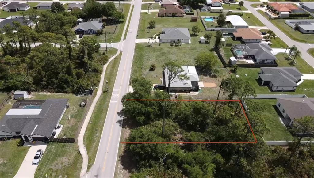 An aerial view shows a vacant, tree-covered residential lot outlined in red next to a road — 23333 QUASAR BOULEVARD, PUNTA GORDA, FL