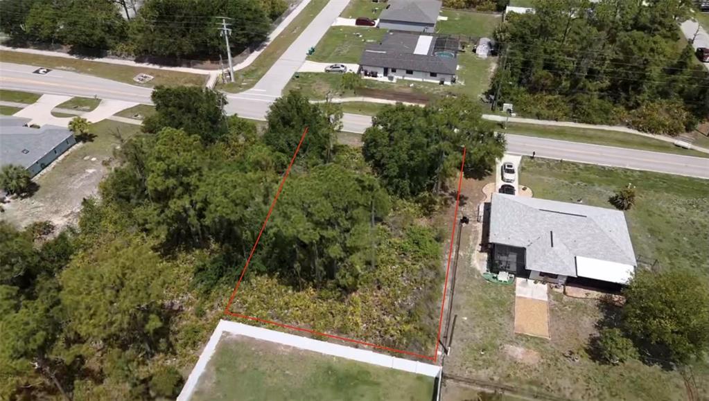 An aerial view shows a vacant, tree-covered residential lot outlined in red between two houses — 23333 QUASAR BOULEVARD, PUNTA GORDA, FL