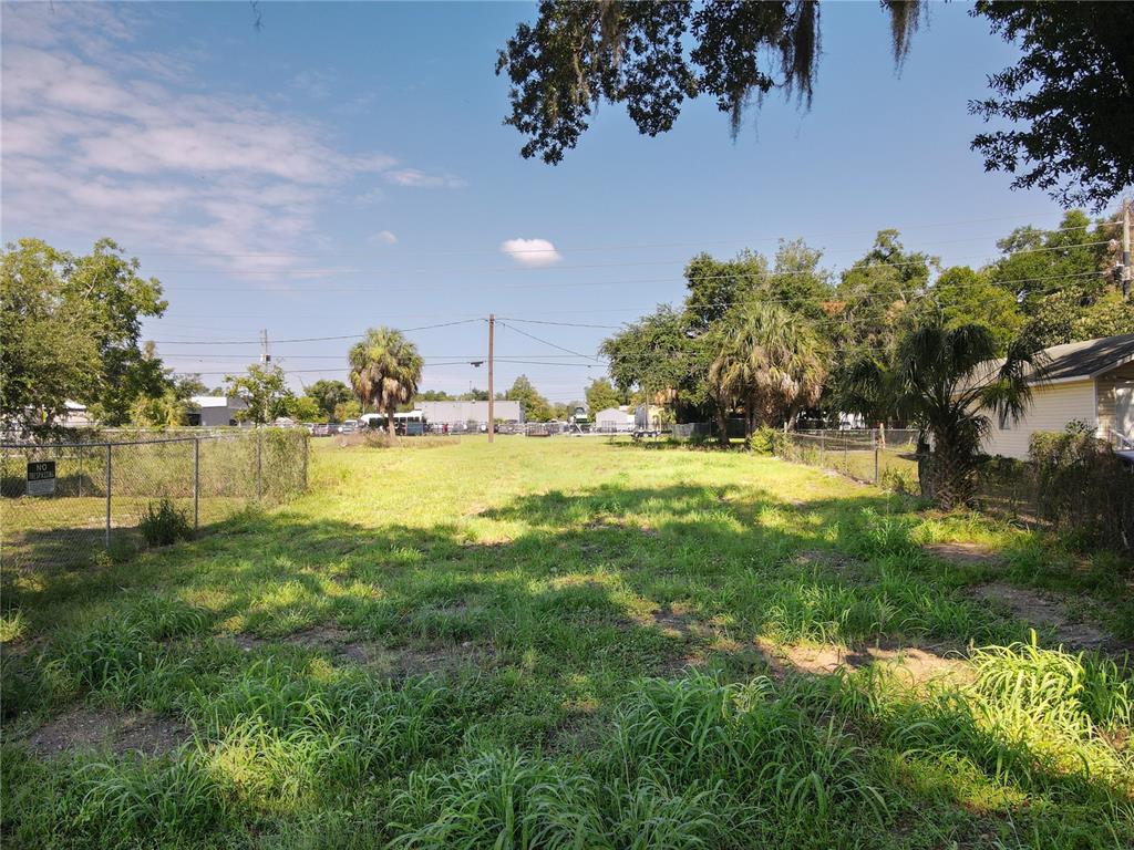 A grassy, vacant lot is enclosed by a chain-link fence with trees in the background — 909 N TENNESSEE AVENUE, LAKELAND, FL