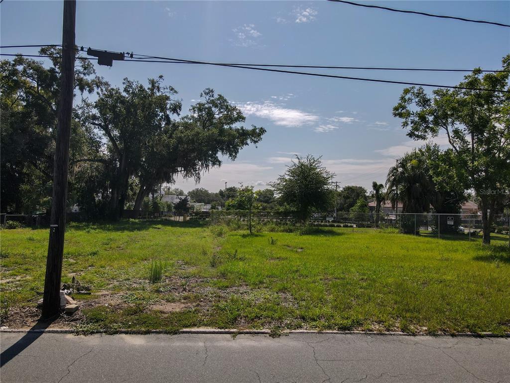 A vacant, grassy residential lot with scattered trees and a chain-link fence in the background — 909 N TENNESSEE AVENUE, LAKELAND, FL