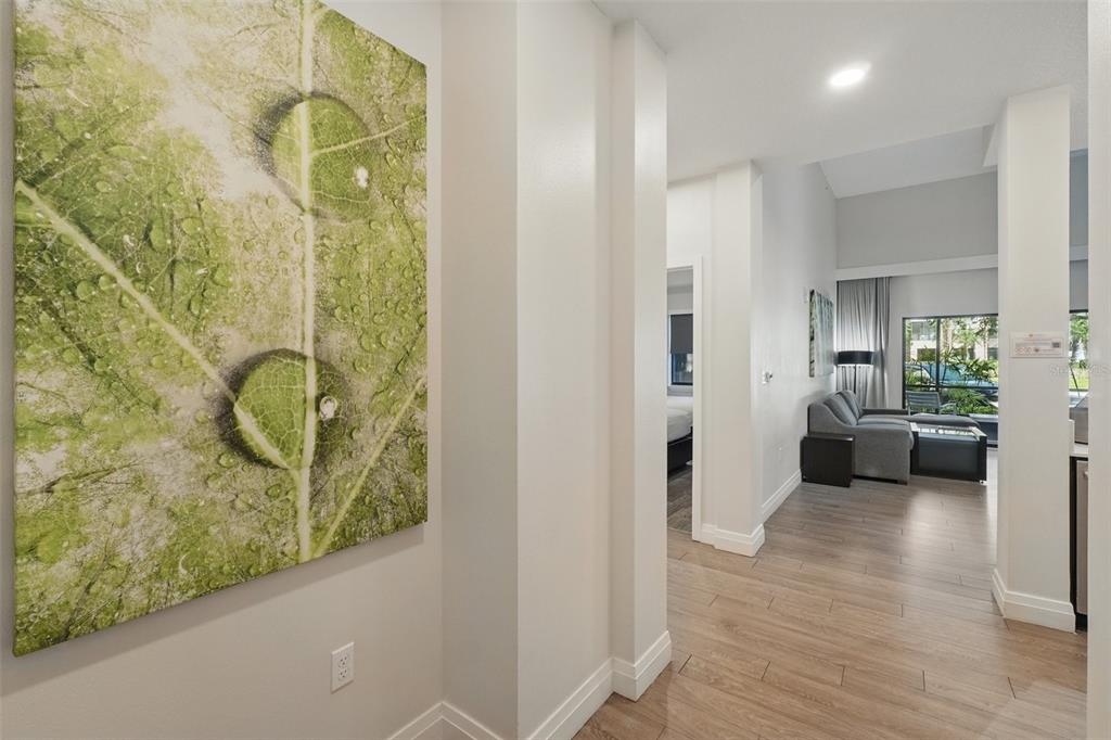 A hallway with a large leaf-themed wall art leads into a living room with wood flooring — 14501 GROVE RESORT AVENUE UNIT 2103, WINTER GARDEN, FL