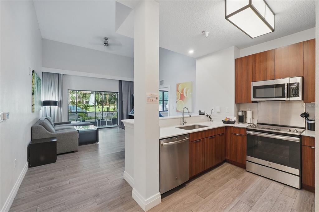 A kitchen with wood cabinets and stainless steel appliances opens to a living room area — 14501 GROVE RESORT AVENUE UNIT 2103, WINTER GARDEN, FL