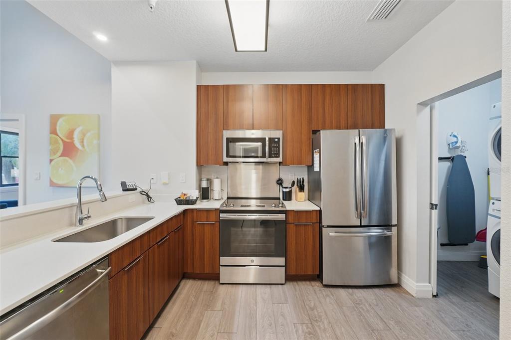 A modern kitchen features wood-toned cabinetry, stainless steel appliances, and white countertops — 14501 GROVE RESORT AVENUE UNIT 2103, WINTER GARDEN, FL