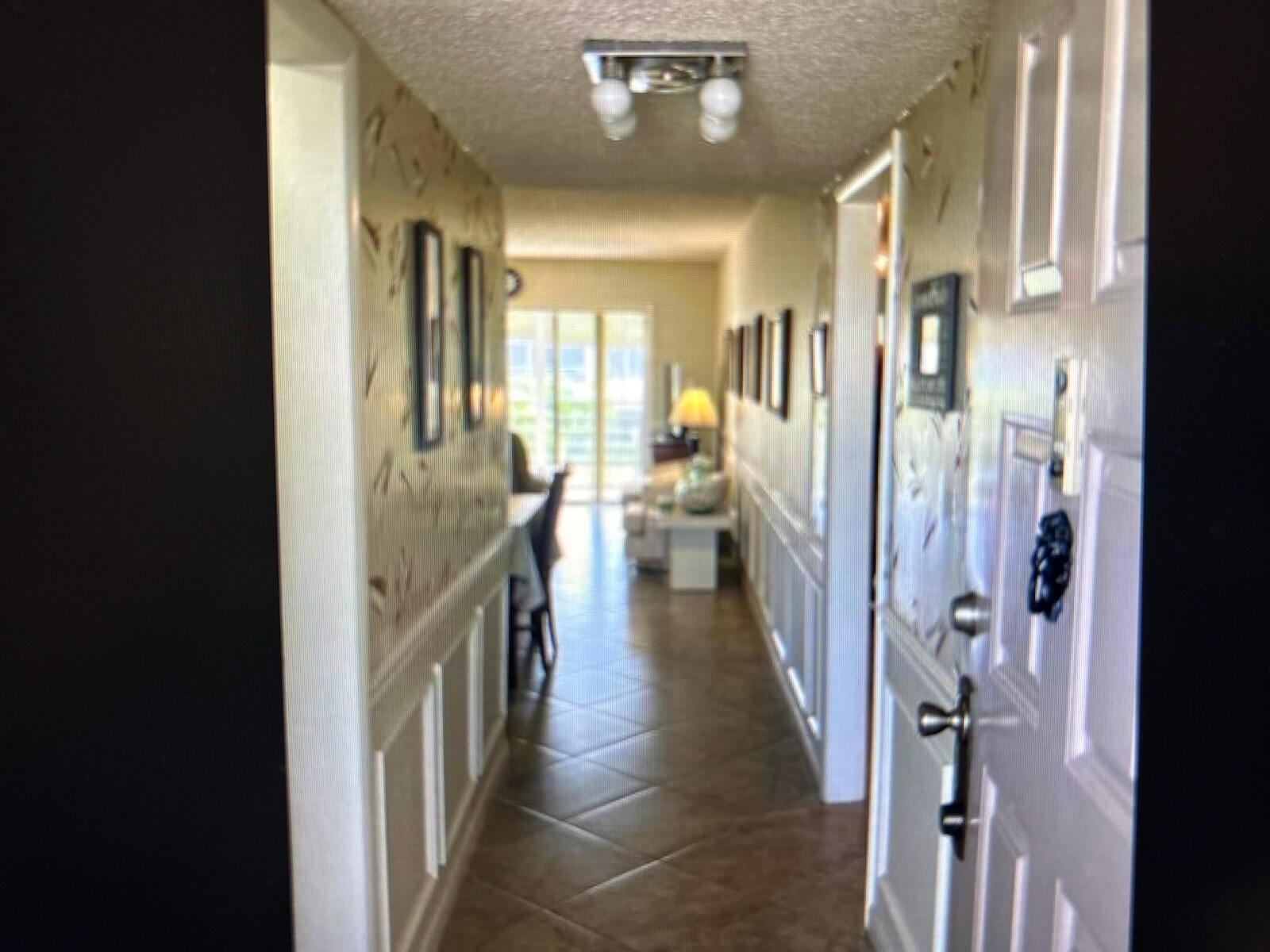 A hallway with patterned wallpaper and wainscoting leads to a living area with tile floors — 3212 Strawflower Way, FL 33467, FL