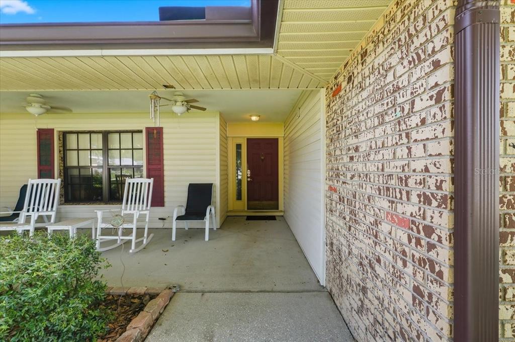 A covered front porch with a brick wall, siding, and a dark red front door — 1700 VARNER COURT, BARTOW, FL
