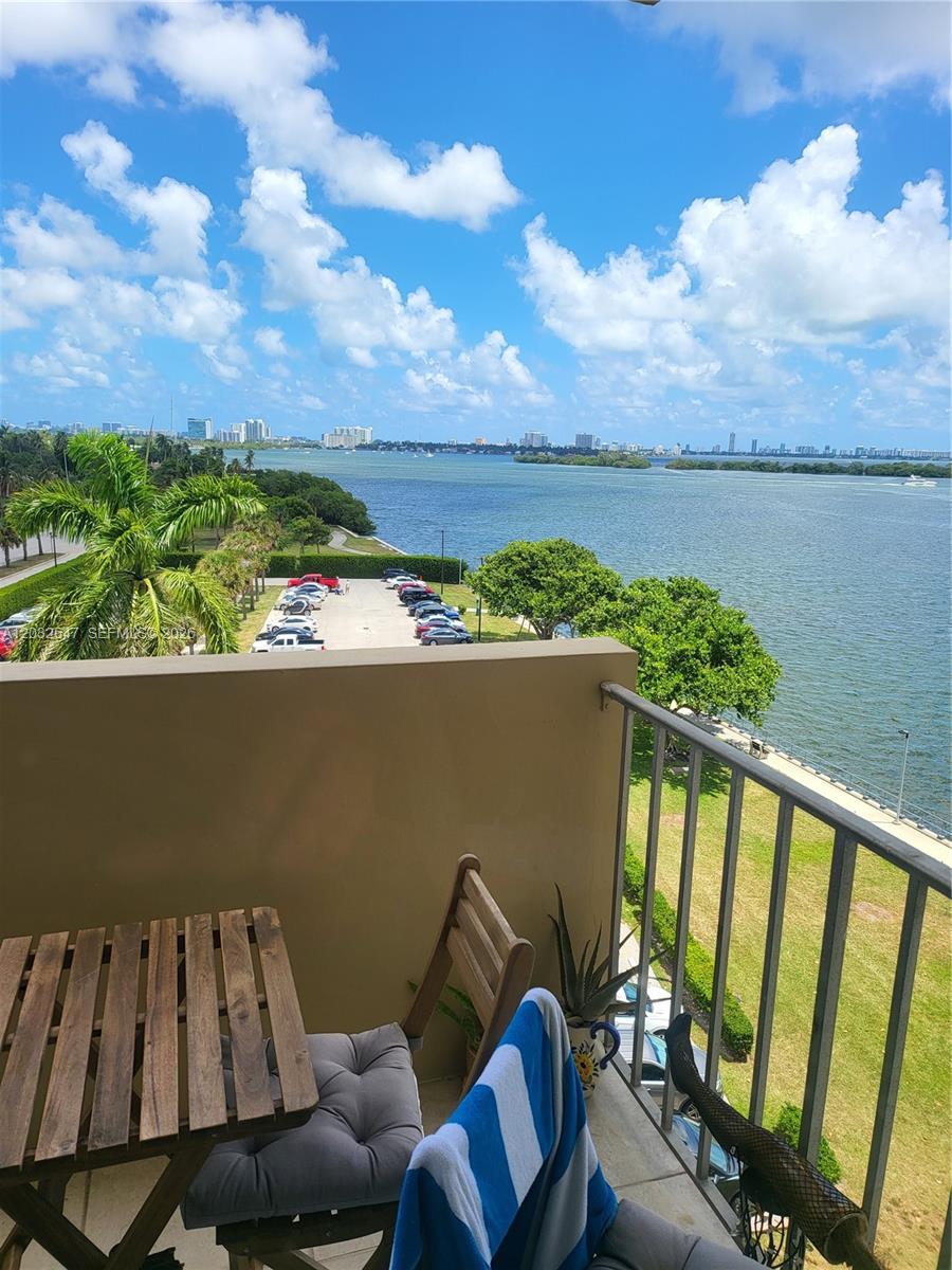 A balcony with a wooden table and chairs overlooks a parking lot and a bay — 880 NE 69th St # 6R, Miami FL 33138, MIAMI, FL
