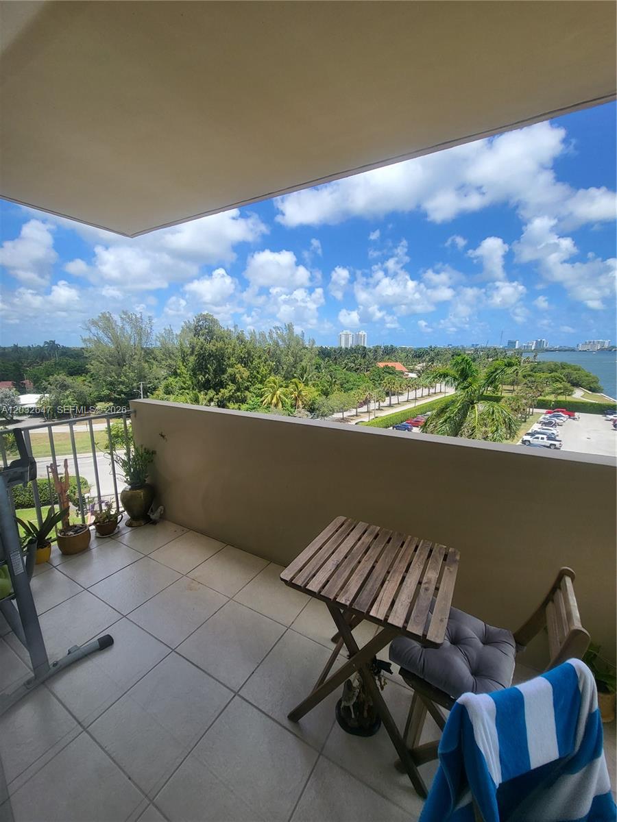 A balcony with tile flooring, a small wooden table, and a view of trees and water — 880 NE 69th St # 6R, Miami FL 33138, MIAMI, FL