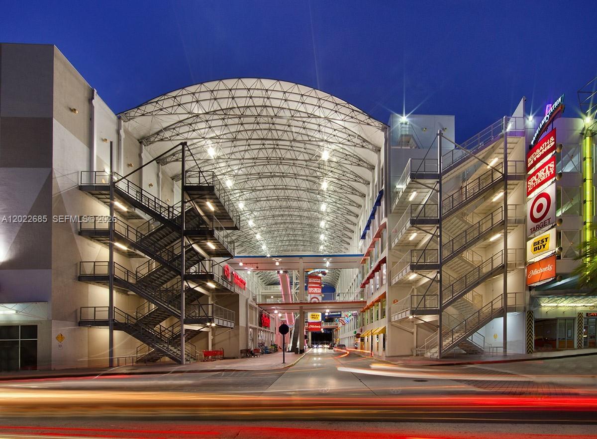 An exterior view of a multi-level shopping center with a large arched roof at night — 9059 SW 73rd Ct, Miami FL 33156, MIAMI, FL
