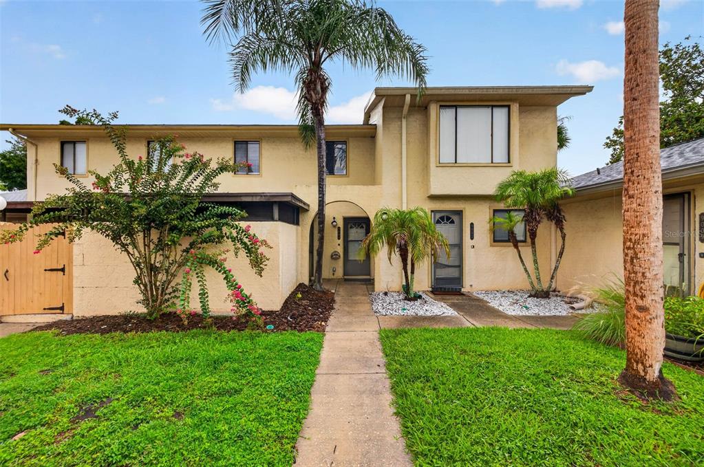 A two-story tan stucco townhouse features a palm tree, a front walkway, and landscaping — 9005 PEBBLE CREEK DRIVE, TAMPA, FL