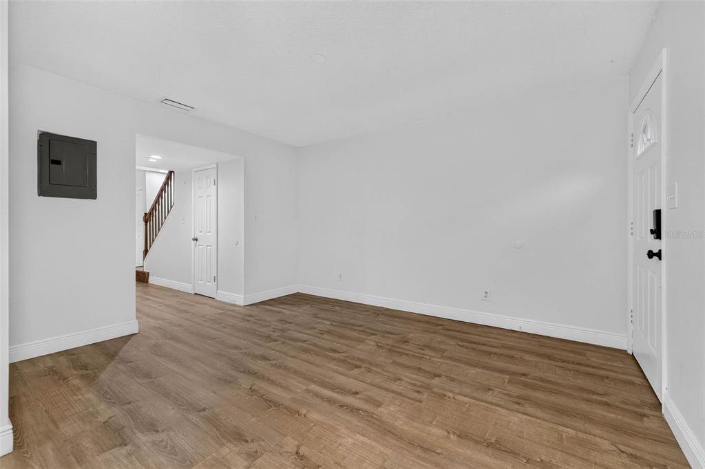 An empty room with light-colored walls, wood-look flooring, a white door, and a staircase visible — 9005 PEBBLE CREEK DRIVE, TAMPA, FL