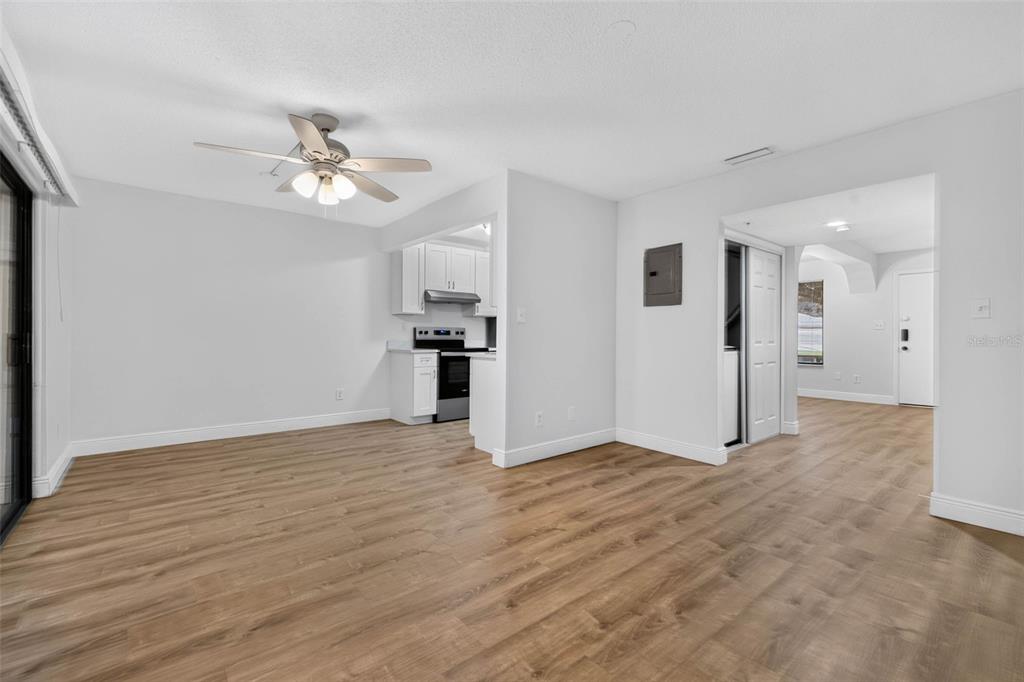 An open-concept living area with light wood-look flooring, white walls, and an adjacent kitchen — 9005 PEBBLE CREEK DRIVE, TAMPA, FL