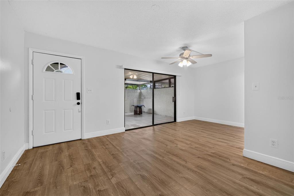A living room with light wood-look flooring, a white front door, and a sliding glass door — 9005 PEBBLE CREEK DRIVE, TAMPA, FL