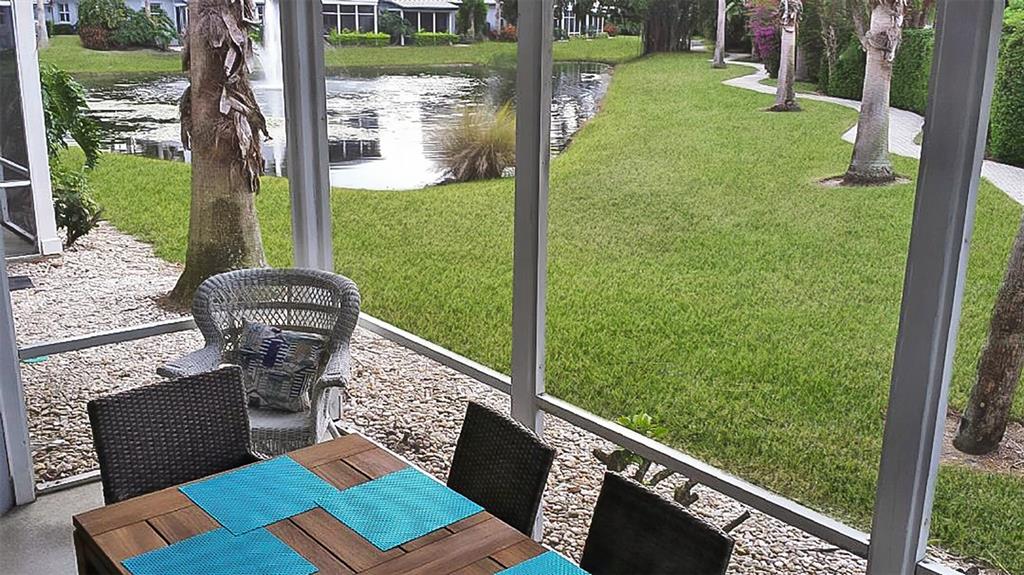 A screened-in patio overlooks a grassy lawn, a pond with a fountain, and palm trees — 1327 SIESTA BAYSIDE DRIVE UNIT 1327-C, SARASOTA, FL