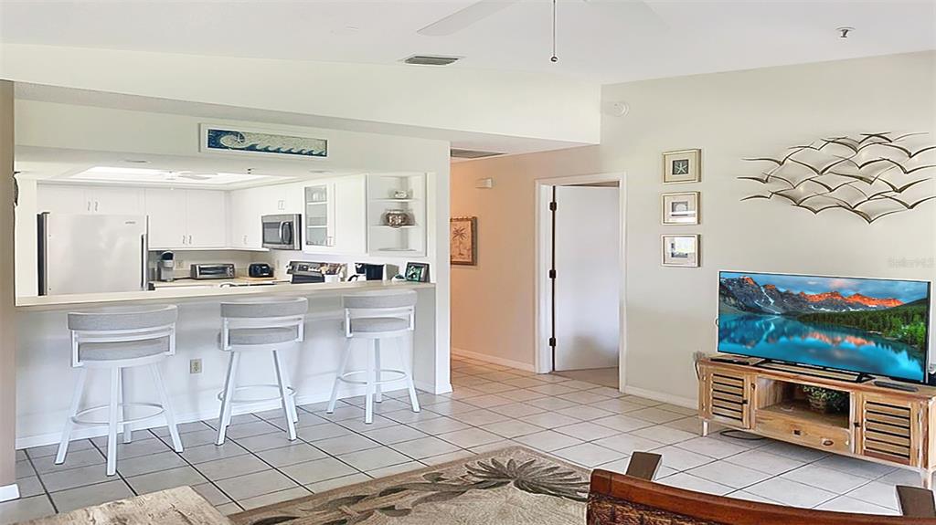 A kitchen with a breakfast bar overlooks a living area featuring a television and tile flooring — 1327 SIESTA BAYSIDE DRIVE UNIT 1327-C, SARASOTA, FL