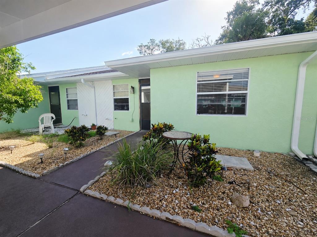 A covered carport with a concrete floor sits in front of a light green house — 6425 DREXEL DRIVE UNIT 2, PORT RICHEY, FL