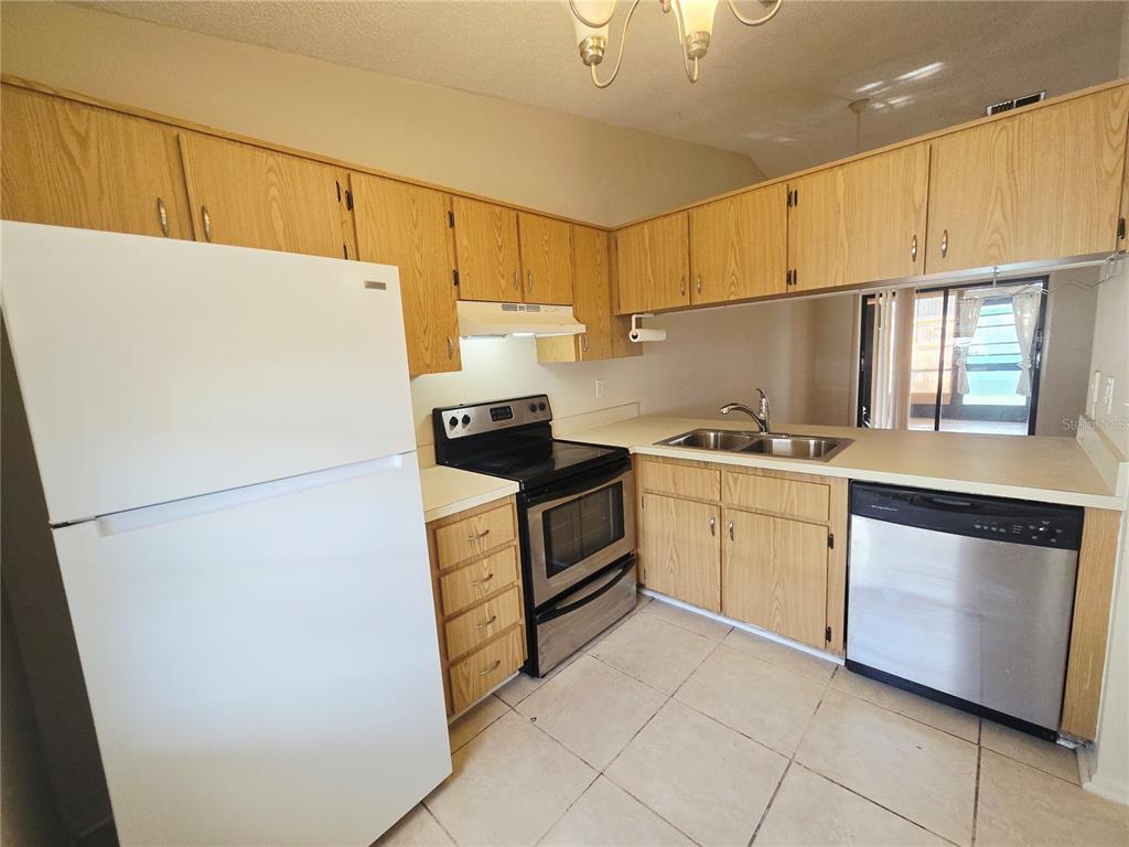 A kitchen features light wood cabinets, a white refrigerator, stainless steel appliances, and tile flooring — 6425 DREXEL DRIVE UNIT 2, PORT RICHEY, FL
