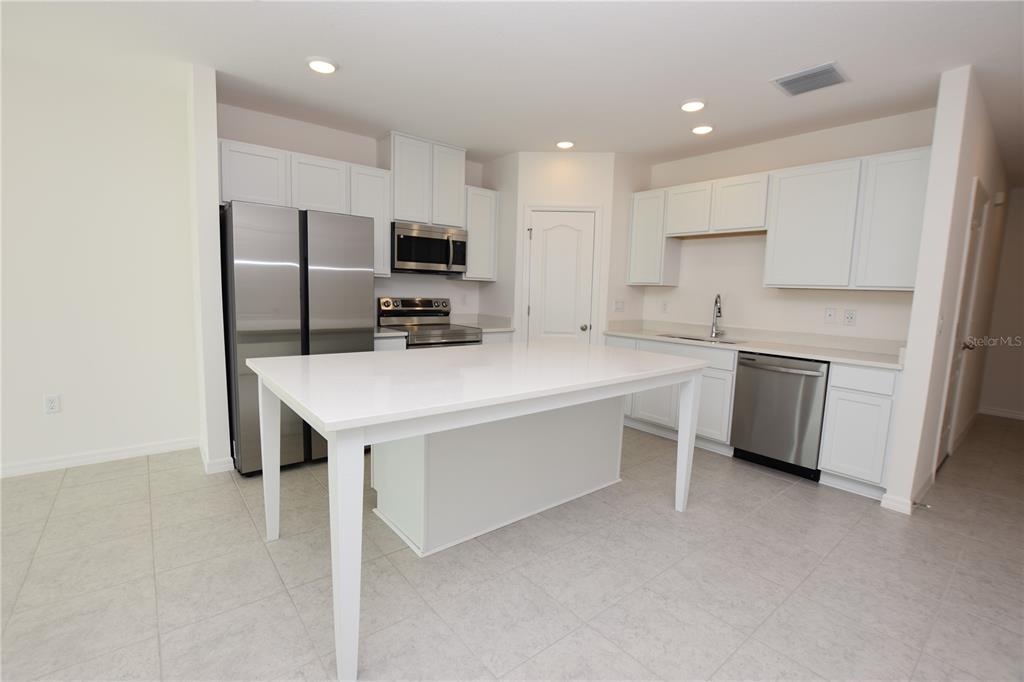 A kitchen features white cabinets, stainless steel appliances, a central island, and light-colored tile flooring — 3905 ACADEMIA AVENUE, LAKELAND, FL