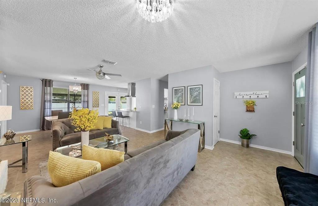 A living room features light gray walls, tile flooring, two gray sofas, and a chandelier — 1121 LONDONDERRY DRIVE, ORANGE PARK, FL
