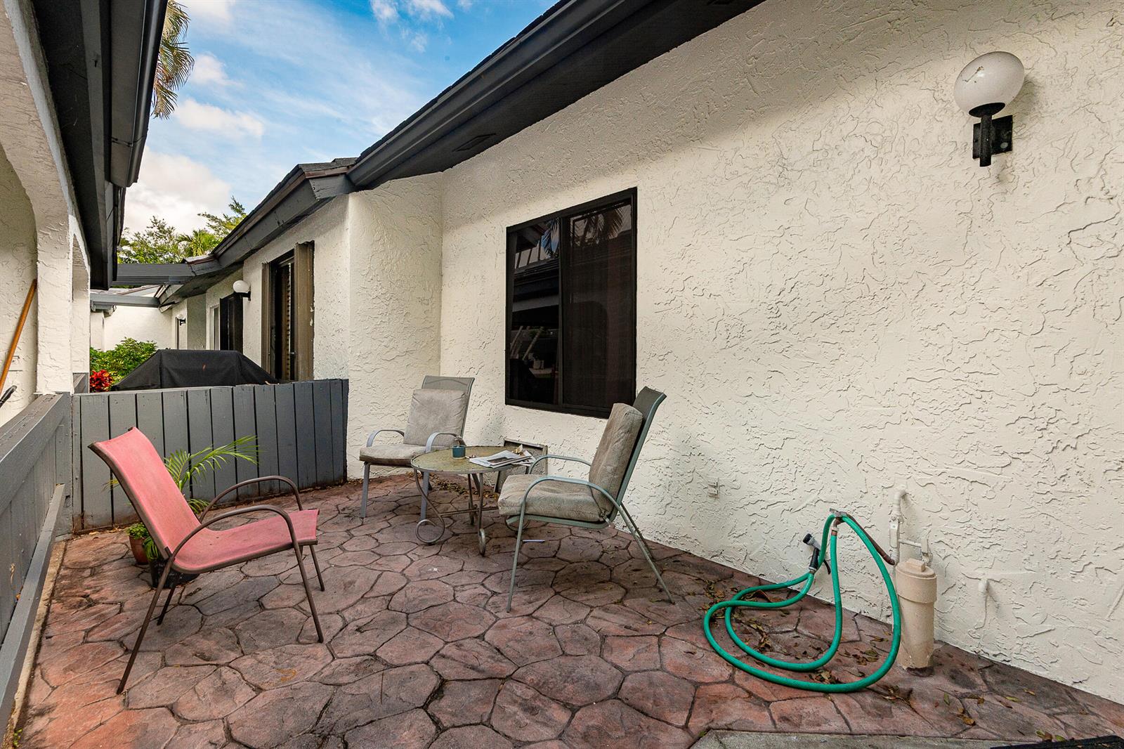 A patio with a textured stone floor, three chairs, a small table, and a garden hose — 10074 Hickorywood Place, Boynton Beach FL 33437, BOYNTON BEACH, FL