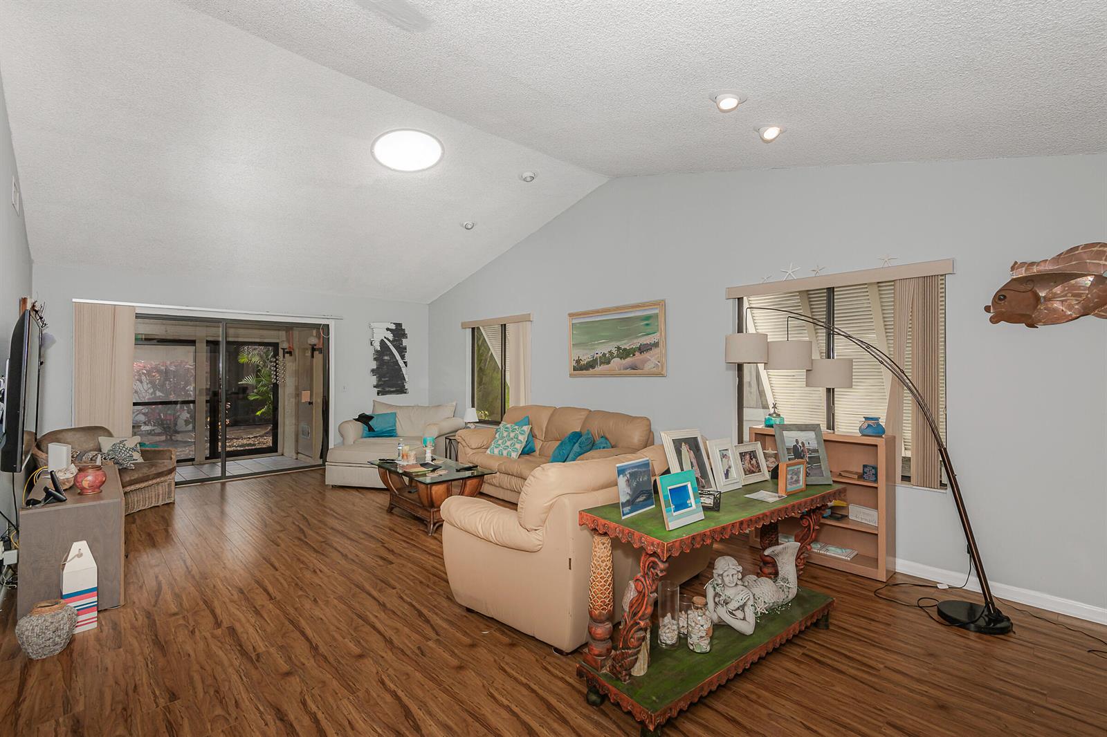 A living room features vaulted ceilings, wood-look flooring, a beige sofa, and a decorative console table — 10074 Hickorywood Place, Boynton Beach FL 33437, BOYNTON BEACH, FL