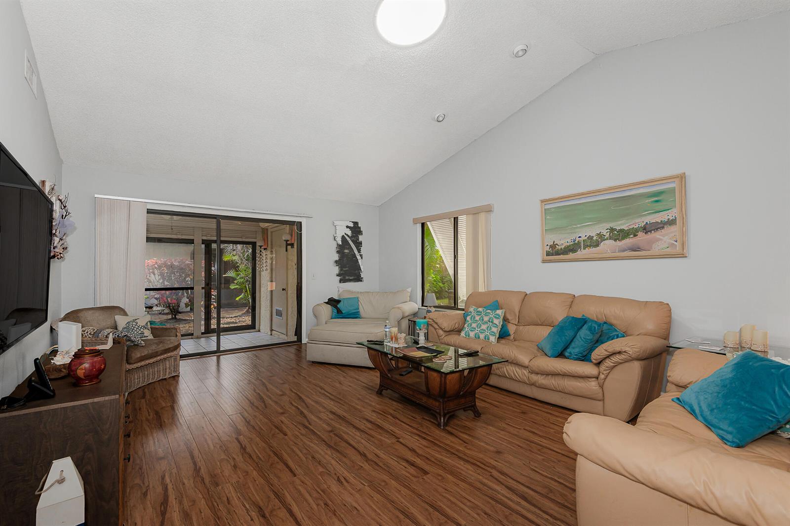 A living room with wood-look flooring, vaulted ceilings, beige leather furniture, and a sliding glass door — 10074 Hickorywood Place, Boynton Beach FL 33437, BOYNTON BEACH, FL
