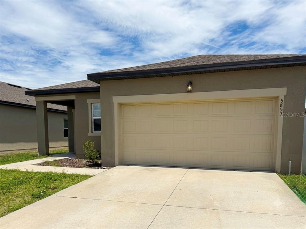 A tan single-story house exterior features a two-car garage and a concrete driveway — 5853 BULLOCK PLACE, ST CLOUD, FL