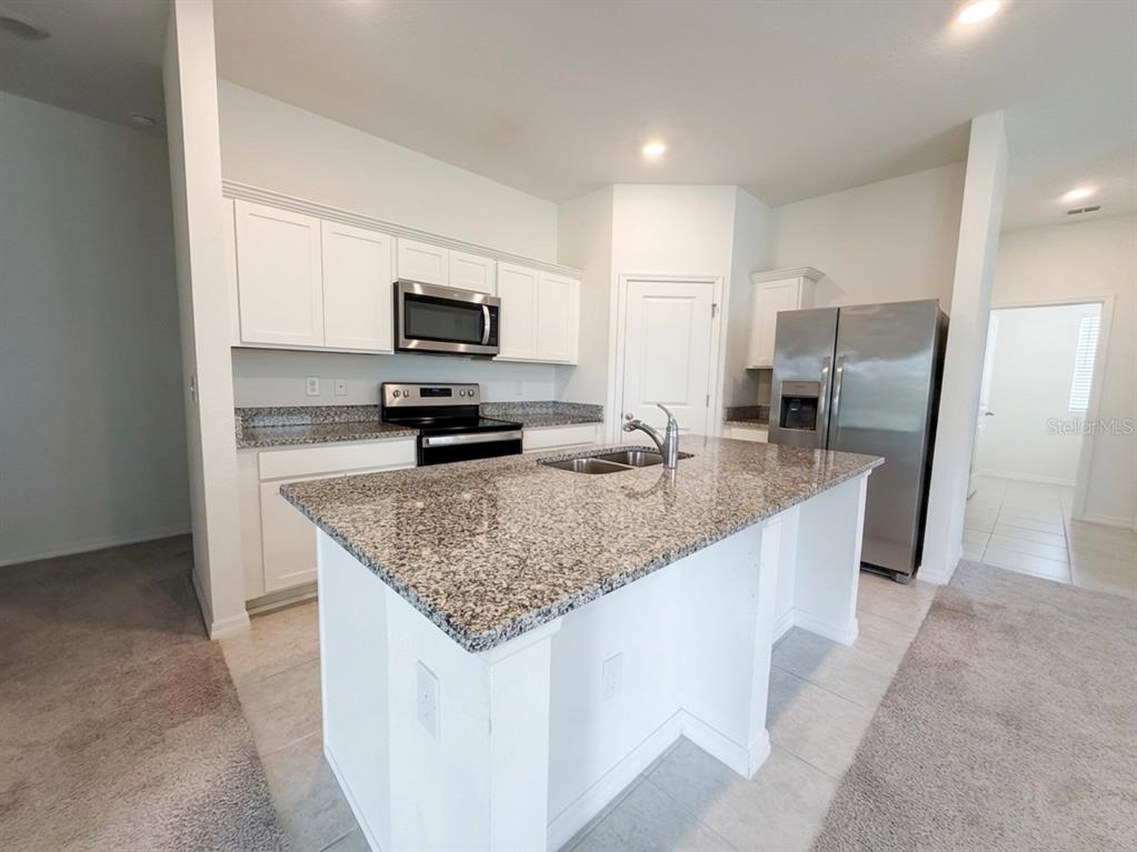 A kitchen with white cabinets, granite countertops, a center island, and stainless steel appliances — 5853 BULLOCK PLACE, ST CLOUD, FL