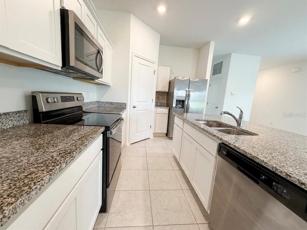 A kitchen features white cabinets, granite countertops, stainless steel appliances, and tile flooring — 5853 BULLOCK PLACE, ST CLOUD, FL