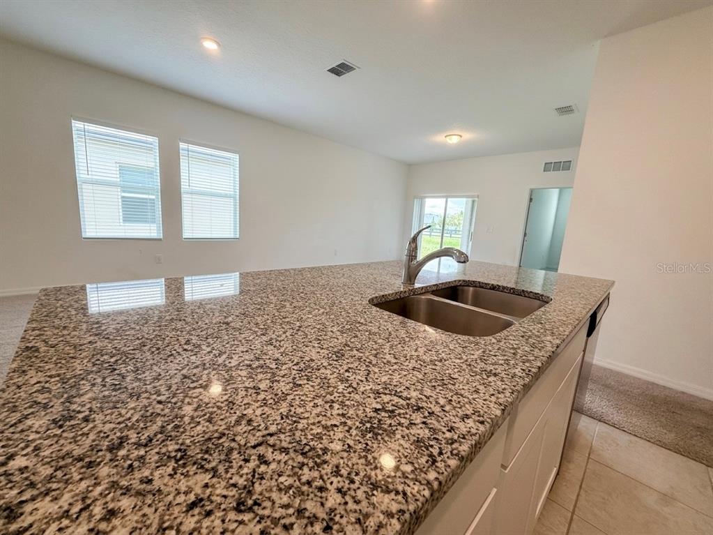 A kitchen island with a granite countertop and stainless steel sink faces an open living area — 5853 BULLOCK PLACE, ST CLOUD, FL