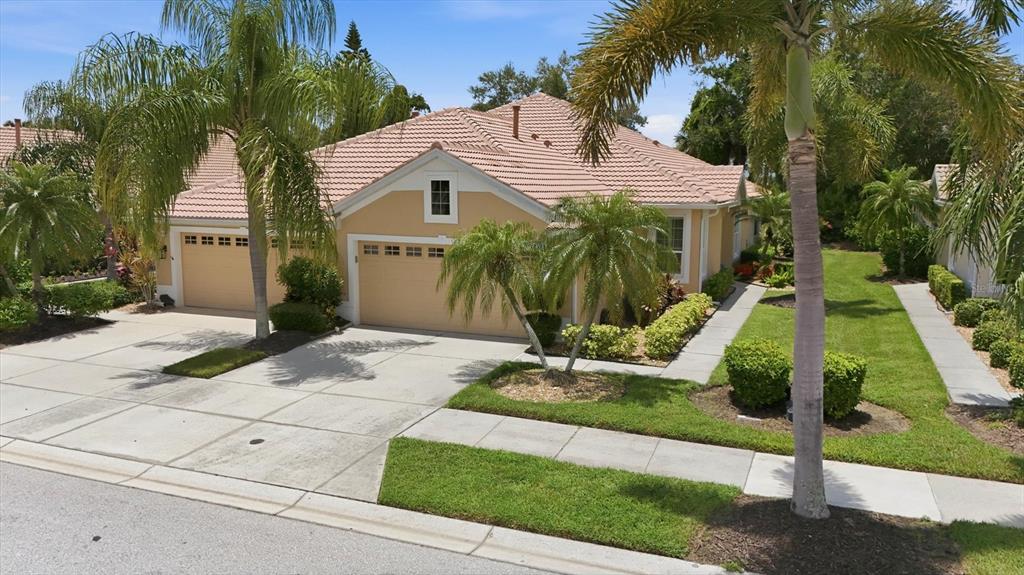 An exterior view of a tan, single-story house with a tile roof and palm trees — 4939 WHISPERING OAKS DRIVE, NORTH PORT, FL