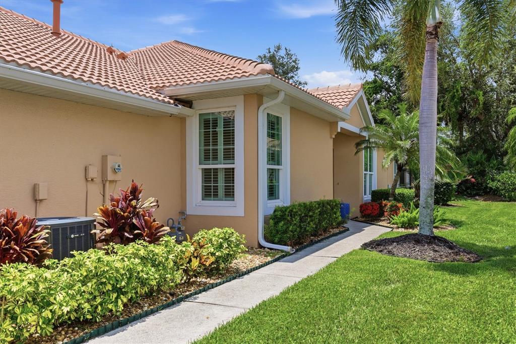 A tan house exterior features a tile roof, a sidewalk, and landscaped bushes and palms — 4939 WHISPERING OAKS DRIVE, NORTH PORT, FL
