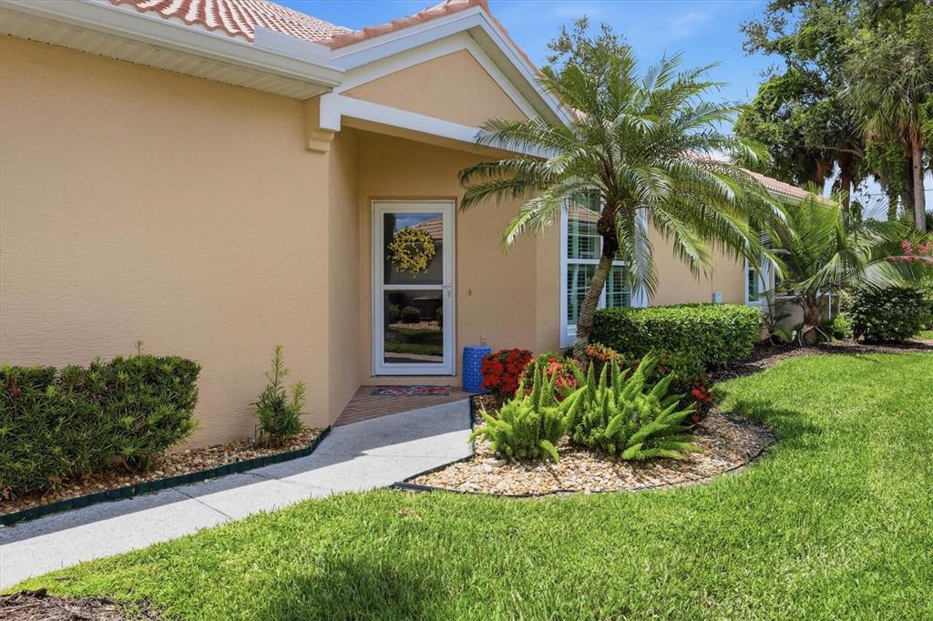 A beige house exterior features a front door, a palm tree, and landscaped garden beds — 4939 WHISPERING OAKS DRIVE, NORTH PORT, FL