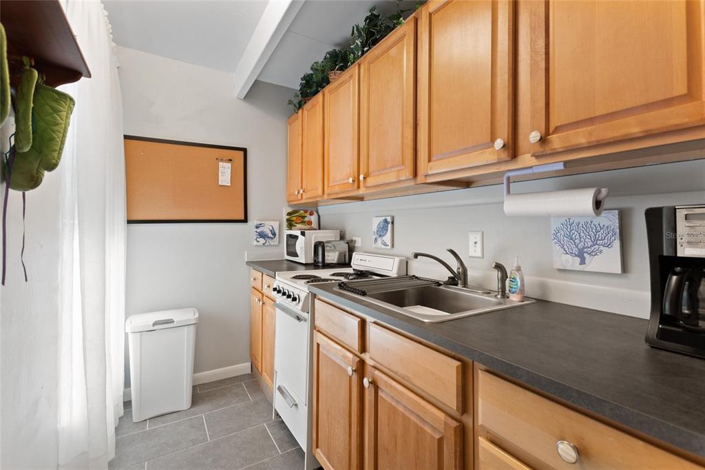 A small kitchen features wooden cabinets, a white stove, a sink, and gray countertops — 1823 CLUB CIRCLE, LAKE WALES, FL