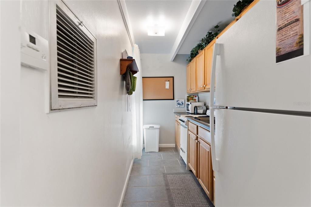 A narrow galley kitchen features light wood cabinets, gray tile flooring, and a white refrigerator — 1823 CLUB CIRCLE, LAKE WALES, FL